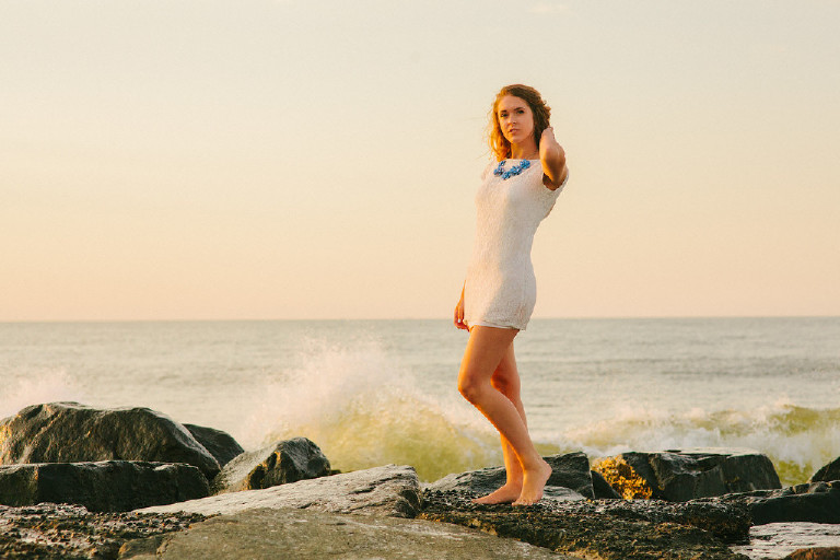 Kaitlyn posing on rock at Asbury Park beach in white dress for Senior Photos with Kasey Ivan Photography