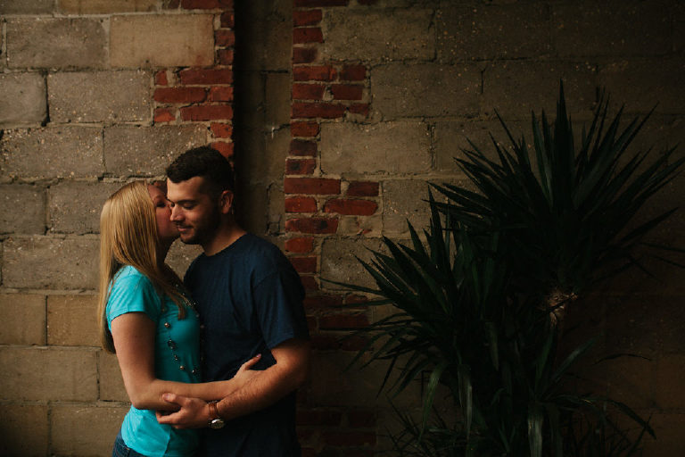 Couple share an intimate kiss by exposed brick inside Capitoline by Bond Street Bar in Asbury Park NJ for engagement photos