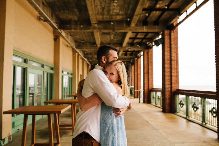 Groom hugs fiance on the Asbury Park beach boardwalk for engagement photos
