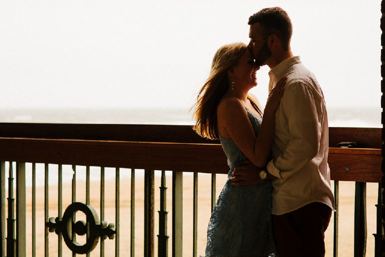 Groom kisses fiance on the forehead as they overlook the Asbury Park beach for engagement photos