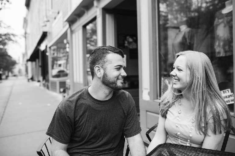 Couple laughs together at a table outside Twisted Coffee in Asbury Park NJ for engagement photos