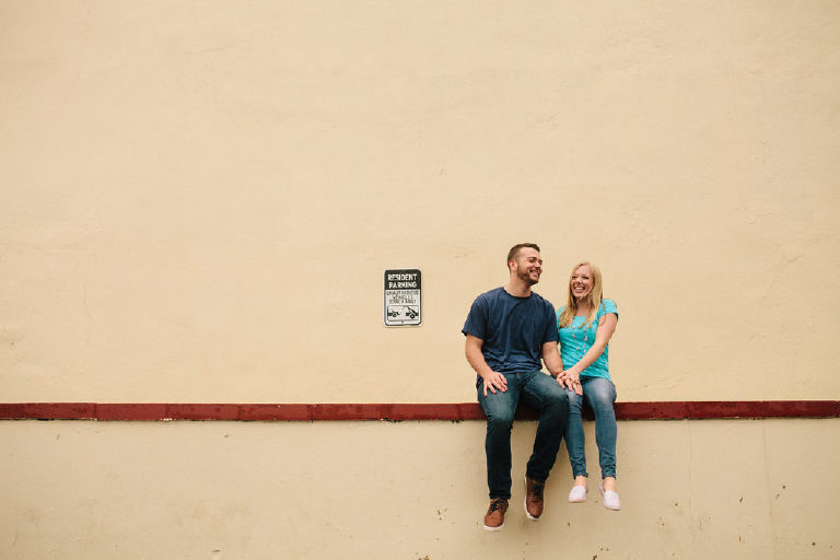Ryan and Jenna laughing on a ledge outside Bond Street Bar in Asbury Park, NJ for engagement photos by Kasey Ivan Photography