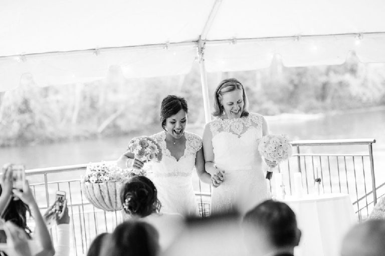 Lesbian brides cheer and dance their way down the aisle of a same sex LGBT wedding at the 1740 House overlooking the Delaware River view by Kasey Ivan
