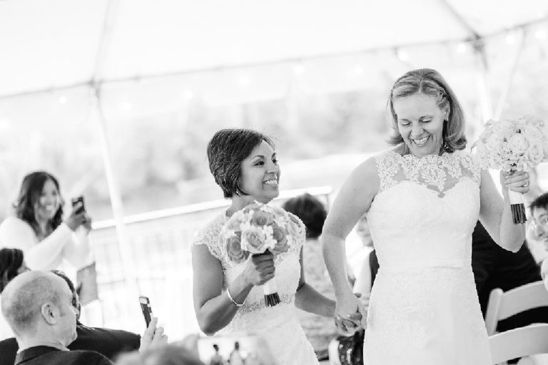 Lesbian brides grin smile and dance their way down the aisle of a same sex LGBT wedding at the 1740 House overlooking the Delaware River view by Kasey Ivan
