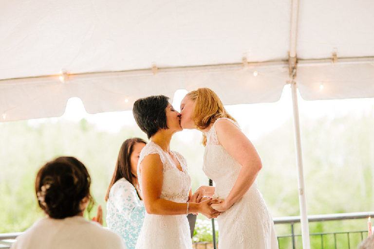brides kiss at the wedding ceremony under the sunlit tent at the 1740 House overlooking the Delaware River