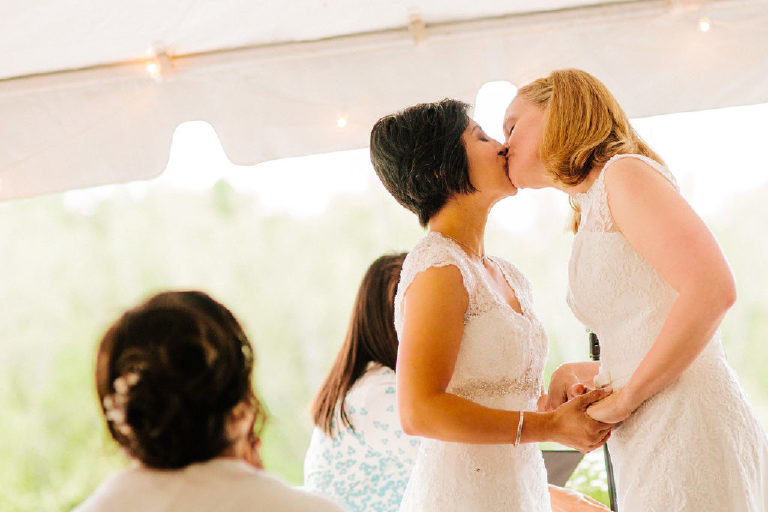 brides kiss at the wedding ceremony under the sunlit tent at the 1740 House overlooking the Delaware River outside New Hope Pennsylvania by Kasey Ivan Photography