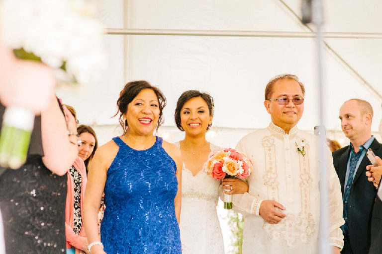 Filipina bride smiles as she walks down the aisle with her parents on each side