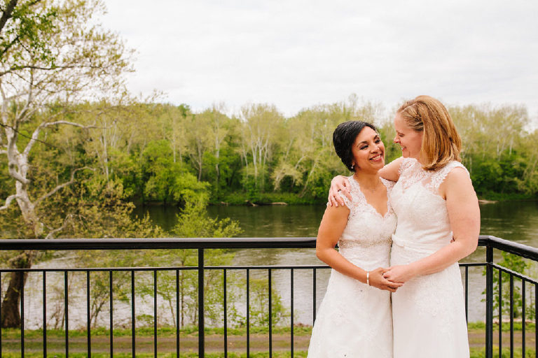 Brides hug each other with a view of the Delaware River from the balcony of 1740 House