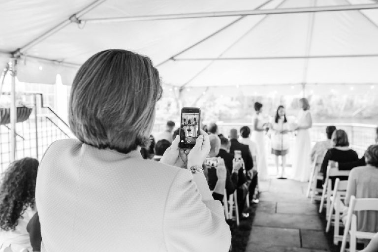 Artistic viewpoint as a guest takes a photo of brides at a same sex lesbian wedding at the Delaware River 1740 House by Kasey Ivan Photography