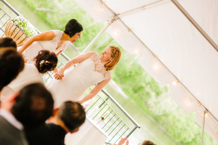 Lesbian brides cheer and dance their way down the aisle of a same sex LGBT wedding at the 1740 House overlooking the Delaware River view by Kasey Ivan
