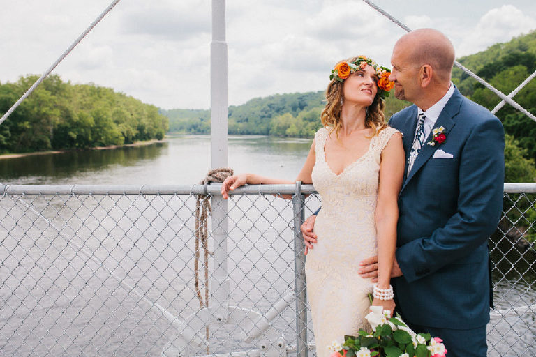 bride and groom smile at each other while standing on a bridge over a view of the Delaware River in summer by Kasey Ivan Photography