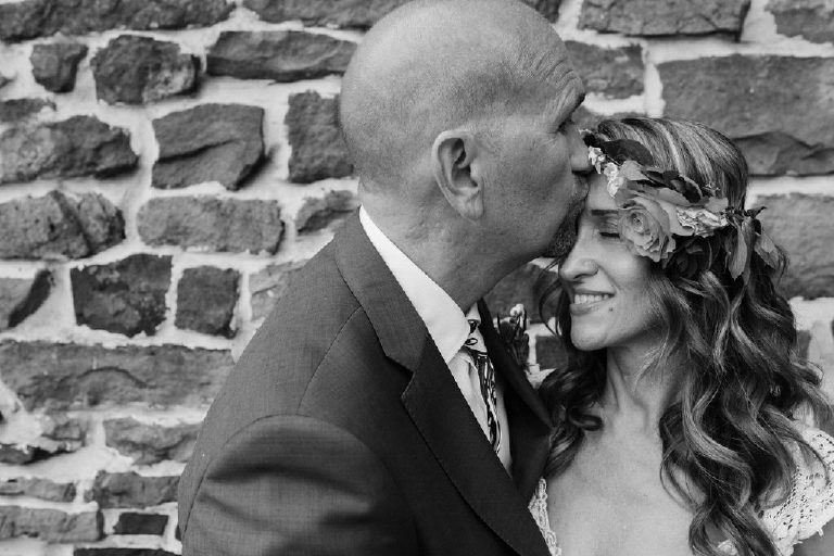 groom kisses bride with flower crown for summer wedding portraits outside a historic stone wall by Kasey Ivan Photography outside the Black Bass Hotel near New Hope PA