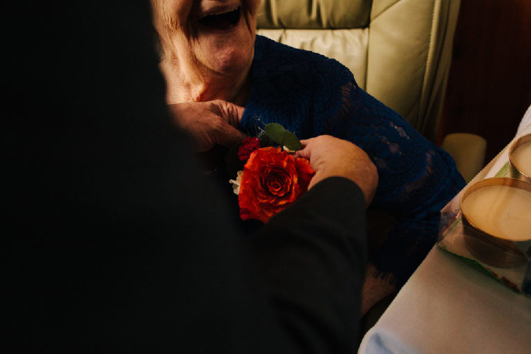mother of the bride laughing while getting a flower pinned on her shirt before wedding