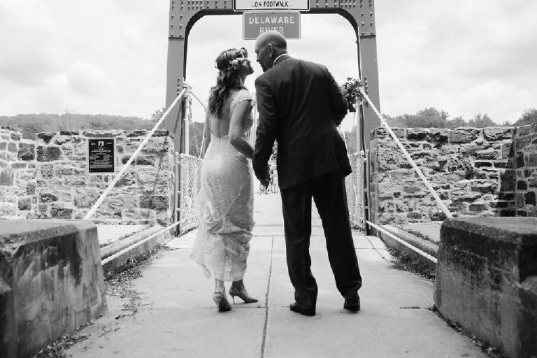 bride and groom hold hands and lean in for kiss before walking onto a bridge over the Delaware River by Kasey Ivan