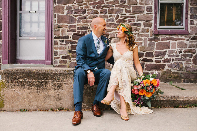 bride with flower crown and groom pose for summer wedding portraits outside a historic stone building near the Lumberville foot bridge over the Delaware River by Kasey Ivan Photography outside the Black Bass Hotel near New Hope PA