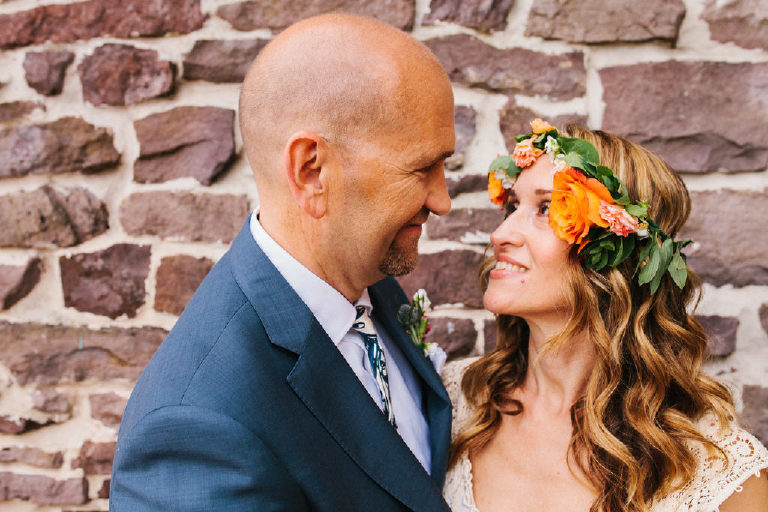bride with flower crown and groom pose for summer wedding portraits outside a historic stone wall by Kasey Ivan Photography outside the Black Bass Hotel near New Hope PA