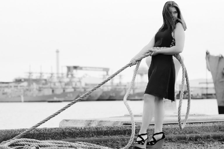 Black and white photograph of a senior girl leaning back and pulling on a rope in the navy shipyard in Philadelphia for Kasey Ivan Photography
