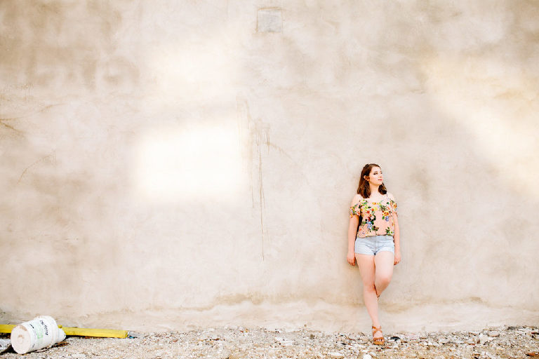 Senior girl posing for photographer leaning on a wall in philadelphia wearing a floral shirt
