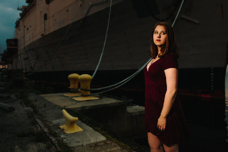 Senior girl standing powerfully wearing a dark purple dress at the navy shipyard in philadelphia posing for Kasey Ivan Photography