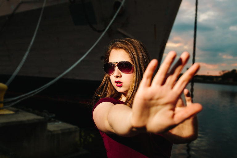 Girl trying to block paparazzi with her hands and sunglasses posing for senior photography for Kasey Ivan Photography
