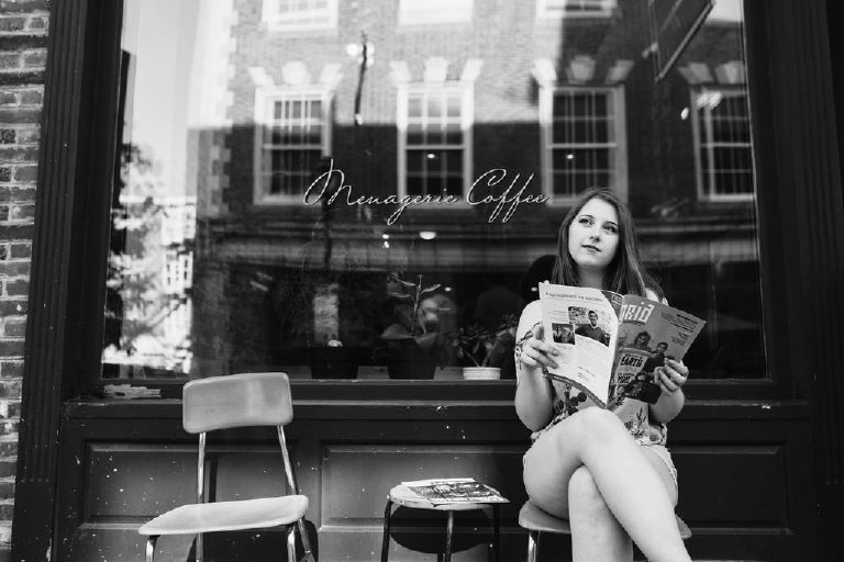 Senior girl sitting outside of a coffee shop on the street thinking with a magazine in old city Philadelphia
