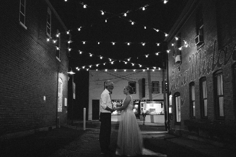 New wife and husband holding hands under string lights at night in a rustic ally Hamilton's Grillroom Lambertville New Hope by Kasey Ivan