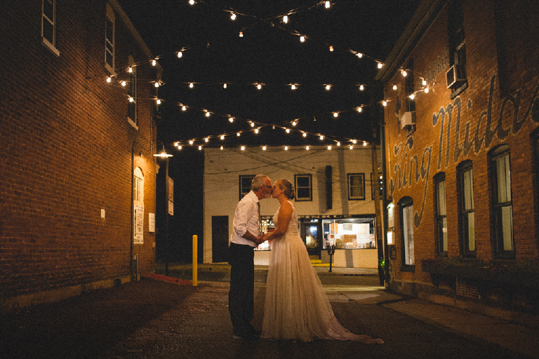 Photograph of husband and wife kissing under string lights in the brick ally of Hamilton's Grillroom Lambertville New Hope by Kasey Ivan
