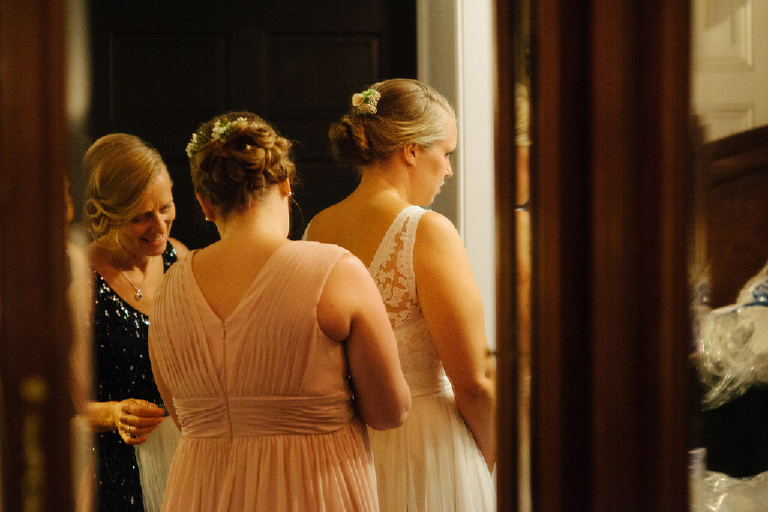 Picture through a mirror of a Women family helping bride get ready for her rustic wedding wearing flowers in her hair