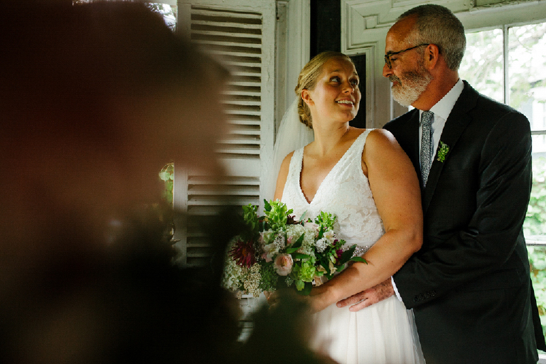 Broom hugging his bride looking at her holding bouquet of flowers