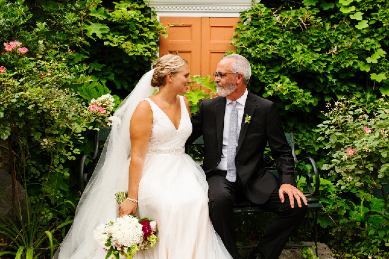 Wife and Husband sitting on a bench on their wedding day in a green garden in the Porches on the Towpath in New Hope and Lambertville
