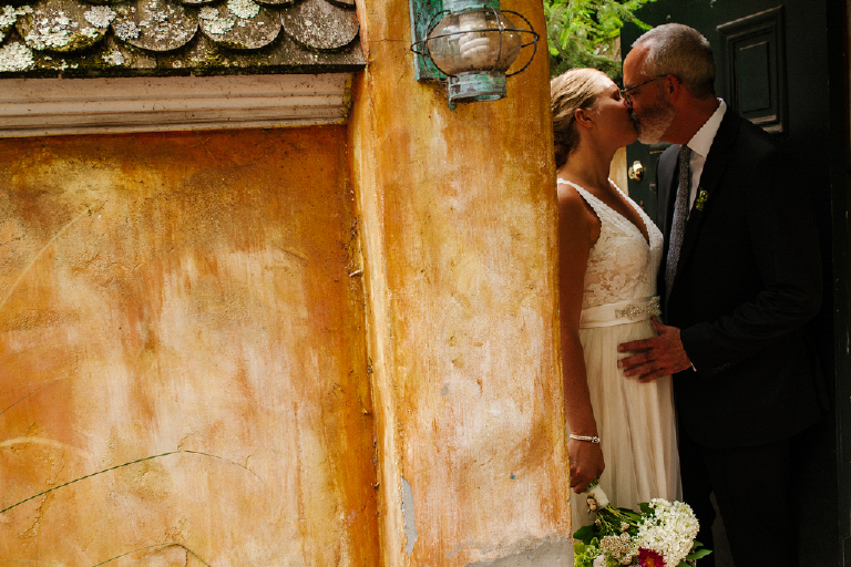 Photograph of a bride and groom leaning against a rustic wall kissing at the Porches on the Towpath in New Hope and Lambertville