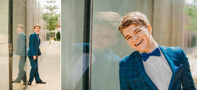 Tyler laughing during senior photos in blue suit on the glass windows at the Michener Museum in Doylestown Pennsylvania by portrait photographer Kasey Ivan Photography