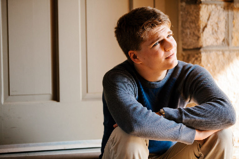 high school boy sits in shade for senior portrait session 