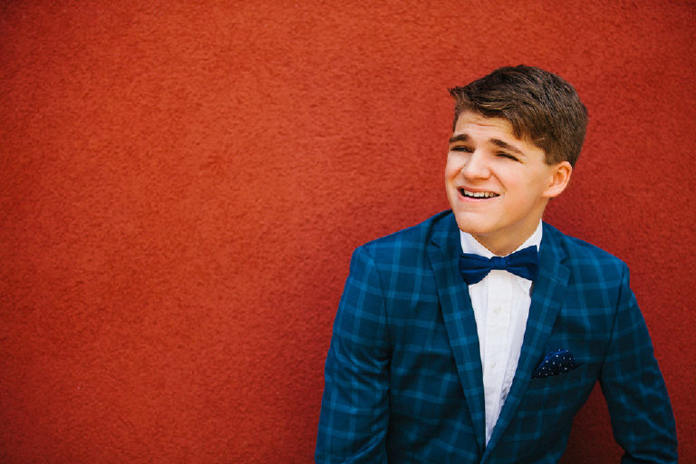 senior photos in blue suit tux in front of red wall at the Michener Museum in Doylestown Pennsylvania by portrait photographer Kasey Ivan Photography