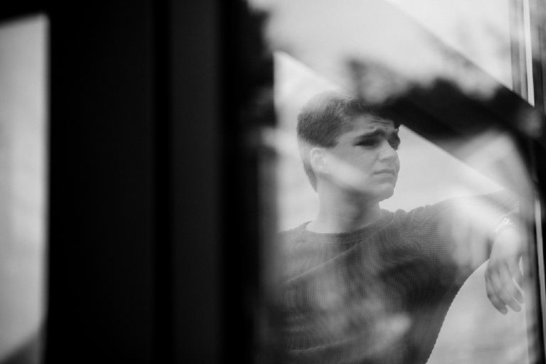 high school senior boy poses outside Mercer Museum in Doylestown Pennsylvania for senior pictures shot through a window by photographer Kasey Ivan Photography
