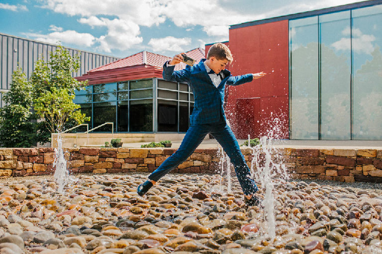 student jumping through fountain for senior photos in blue suit at Michener Museum in Doylestown Pennsylvania by portrait and fashion photographer Kasey Ivan Photography