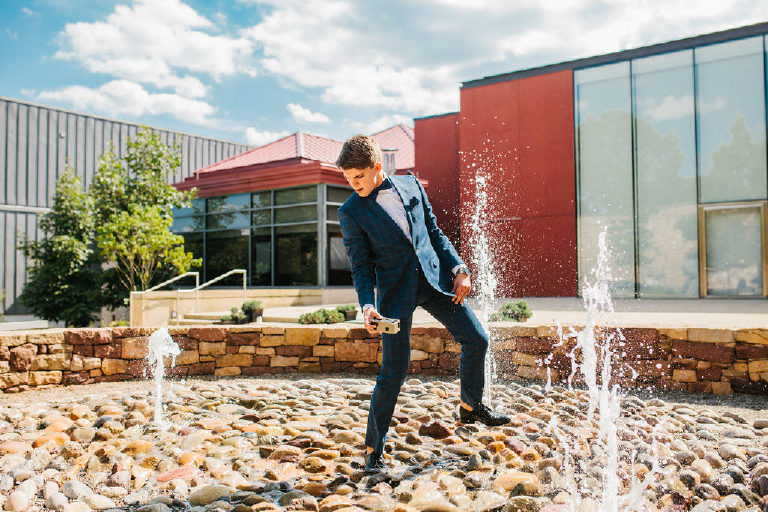 student dancing in fountain for senior photos in blue suit at Michener Museum in Doylestown Pennsylvania by portrait photographer Kasey Ivan Photography