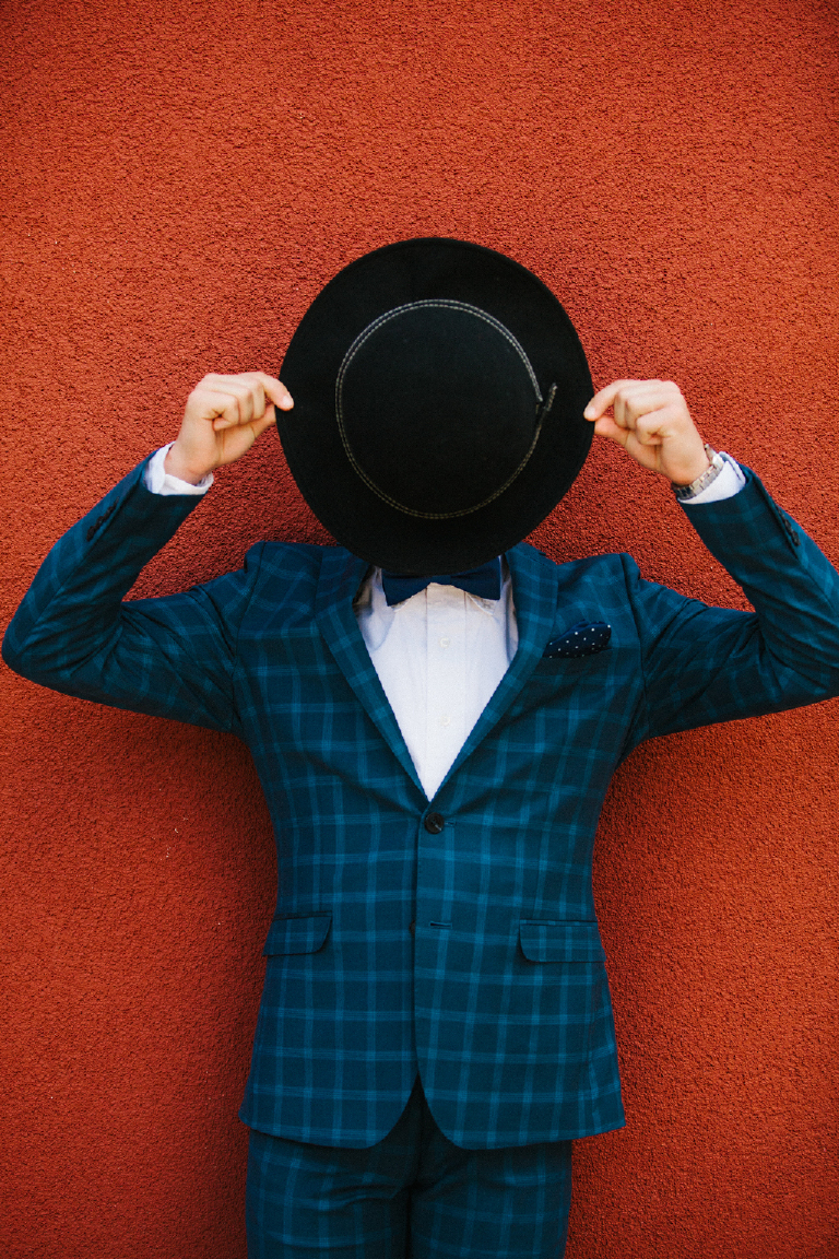 funny senior photo of blue suit and black hat covering the face by photographer Kasey Ivan Photography