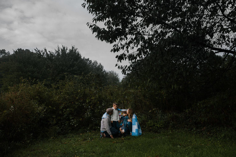 family huddles under blanket in woods for family portrait by New Hope photographer Kasey Ivan