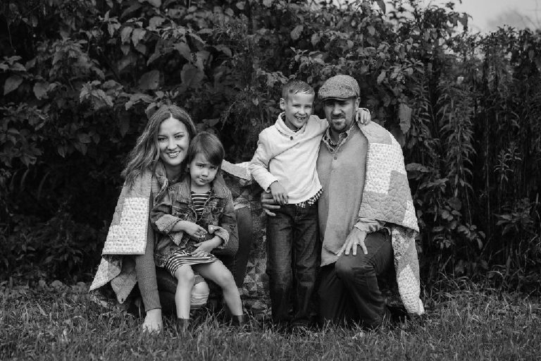 family huddles under blanket in woods for family portrait by New Hope photographer Kasey Ivan