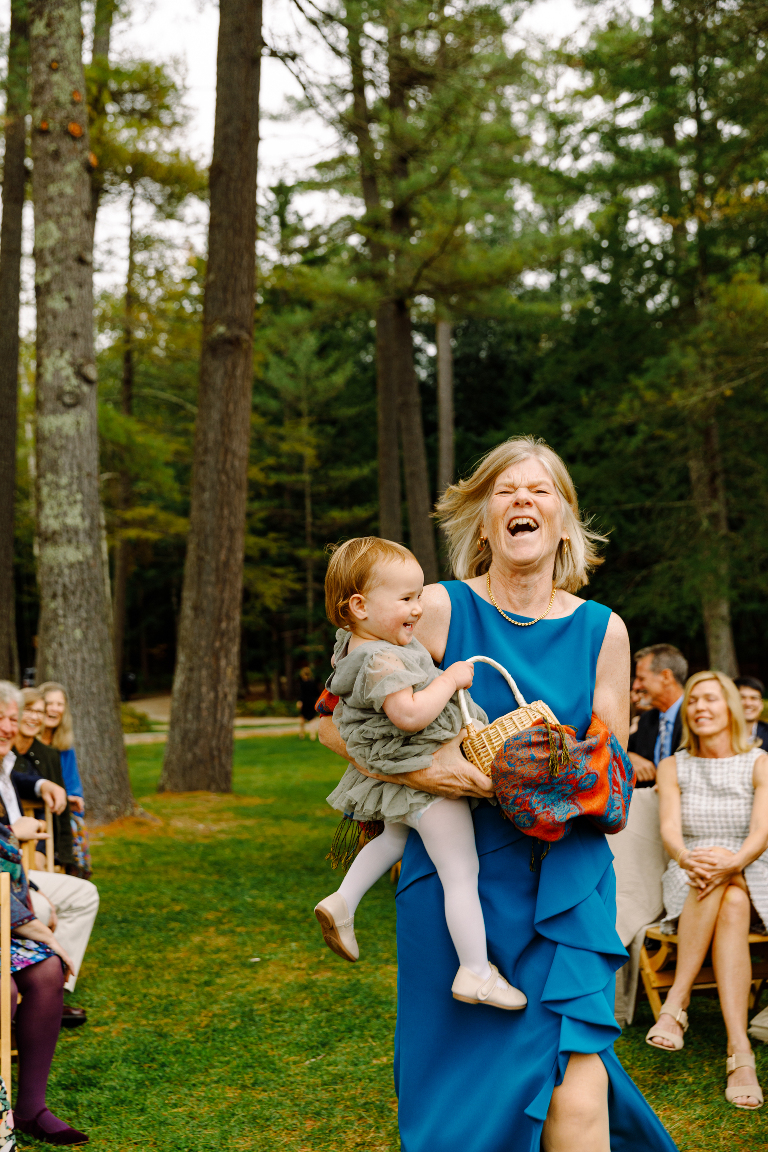 Mother of the bride laughing with the flower girl as they walk down the aisle to the wedding ceremony at the Tarry A While Resort in Bridgton Maine.