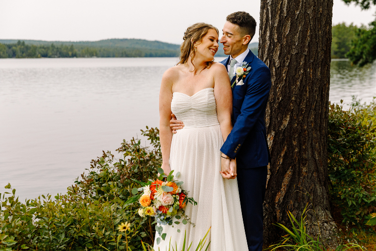 Bride and groom smiling and holding hands near the lake for their couples wedding photos at the Tarry A While Resort in Bridgton Maine