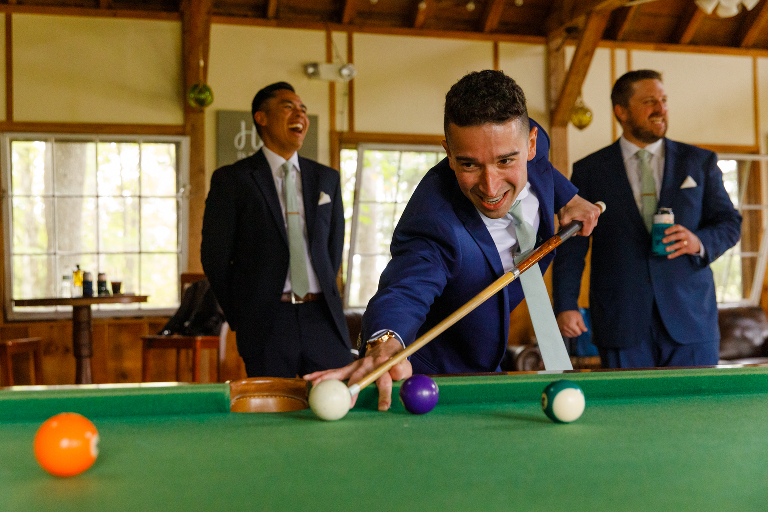 Groom and his groomsmen laughing and playing pool before a wedding at Tarry A While Resort
